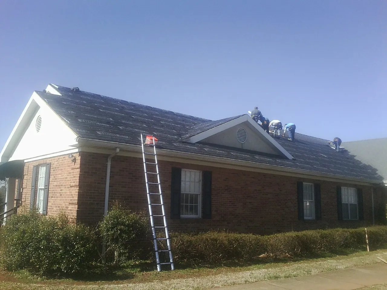 Crew tearing shingles off a brick ranch roof with a ladder set — Emergency Roof Repair work by our crew in Boothbay Harbor