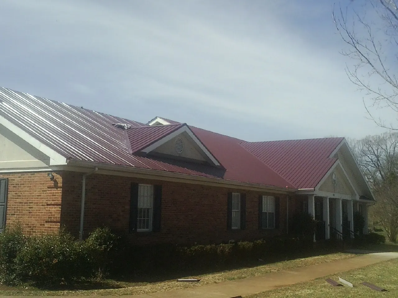 Red metal roof with gabled entries on a long brick building, from a Hail Damage Roof Repair job in Boothbay Harbor