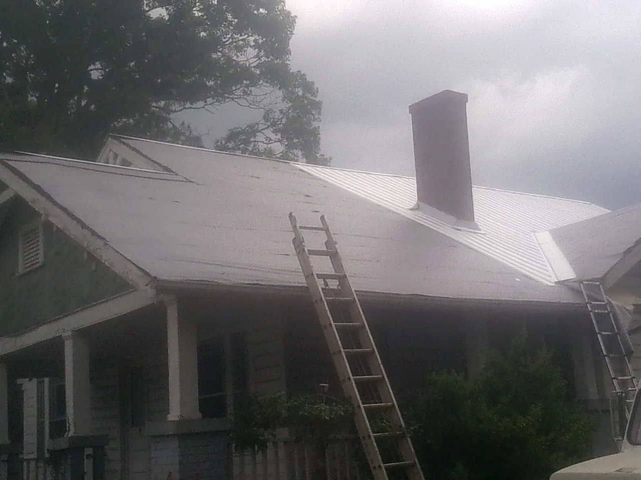 Ladders against a metal roof on an older home with a brick chimney in Boothbay Harbor