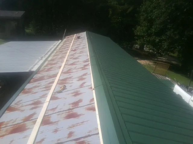 Old rusted panels beside newly installed green metal roofing — Wind Damage Roof Repair by Roofing Brothers in Boothbay Harbor