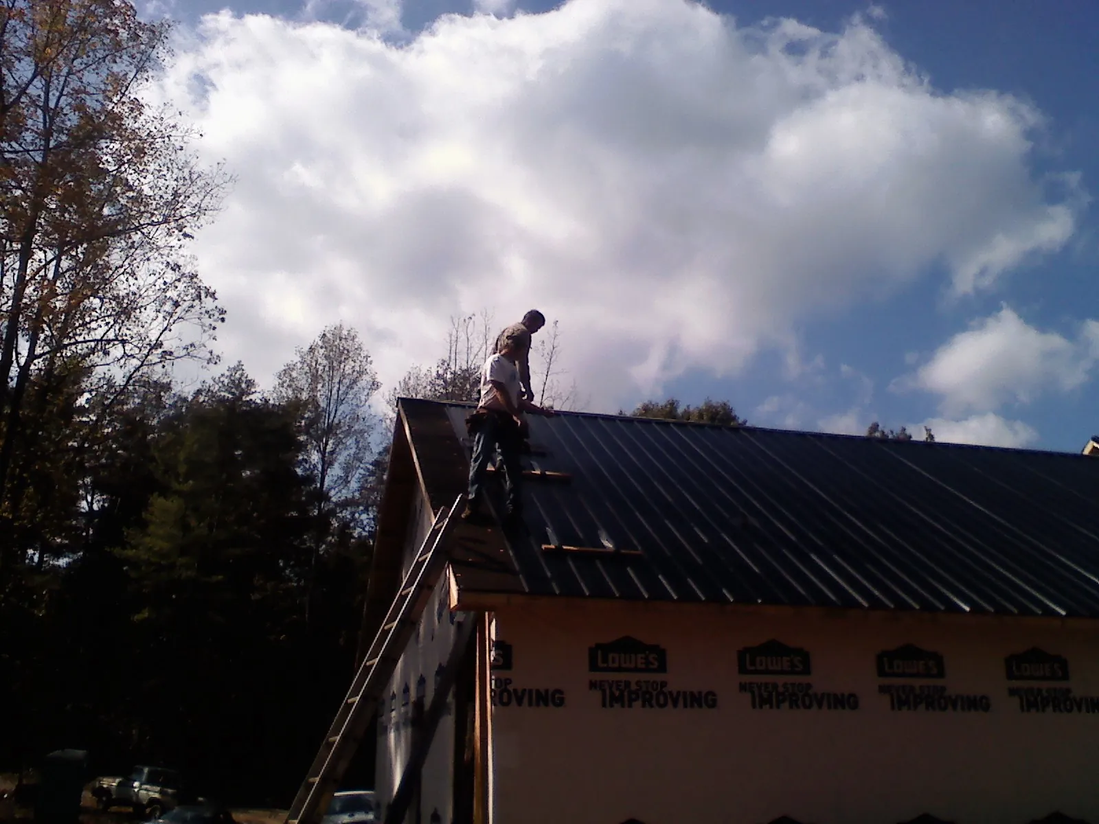 Roofer fastening dark metal panels high against a cloudy sky, from a Roof Inspection job in Boothbay Harbor
