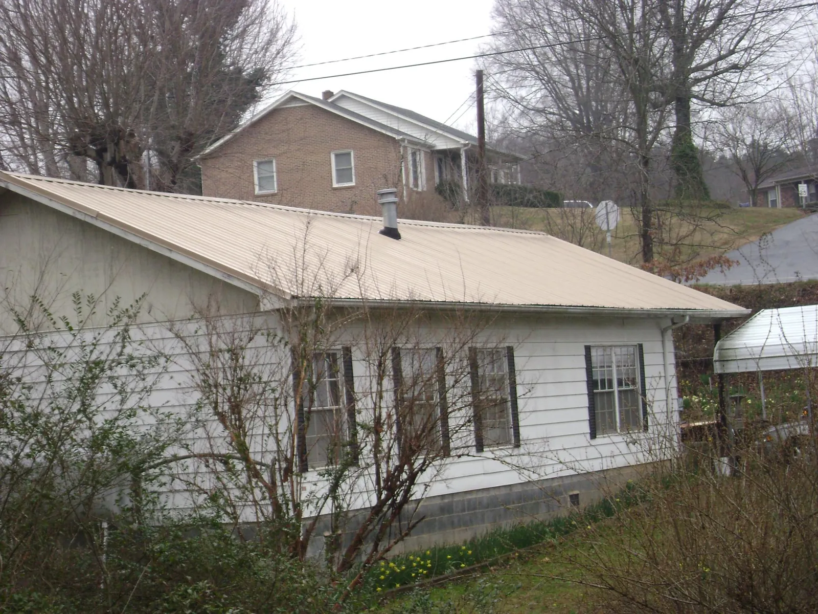 Tan metal roof on a white sided house set into a hillside — Commercial Roofing by Roofing Brothers in Boothbay Harbor