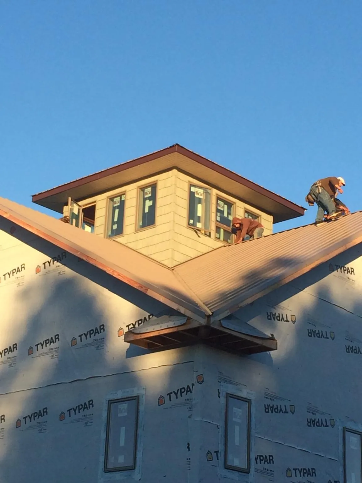 Roofers working around a rooftop cupola on a new metal roof at sunset — Roof Waterproofing in Boothbay Harbor by Roofing Brothers